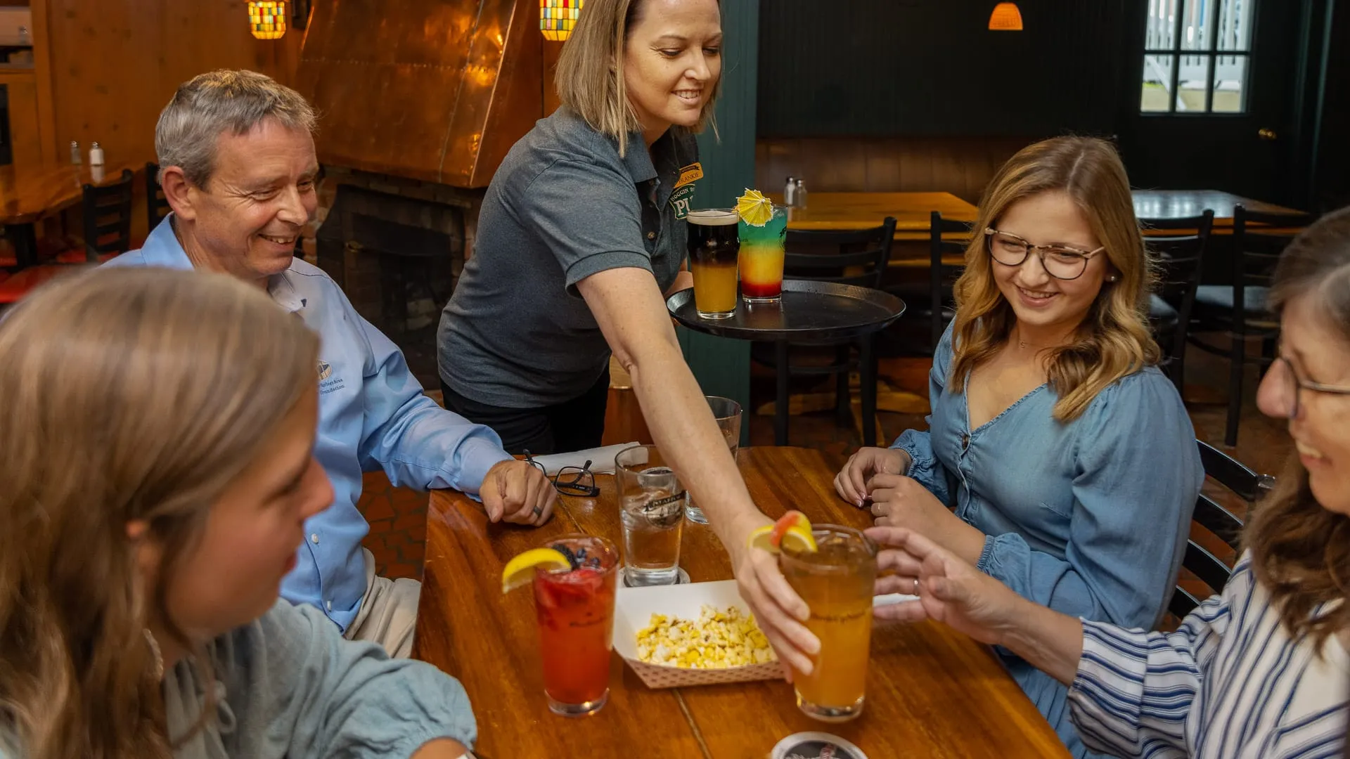 A group of people at dinner with their waitress putting down drinks.