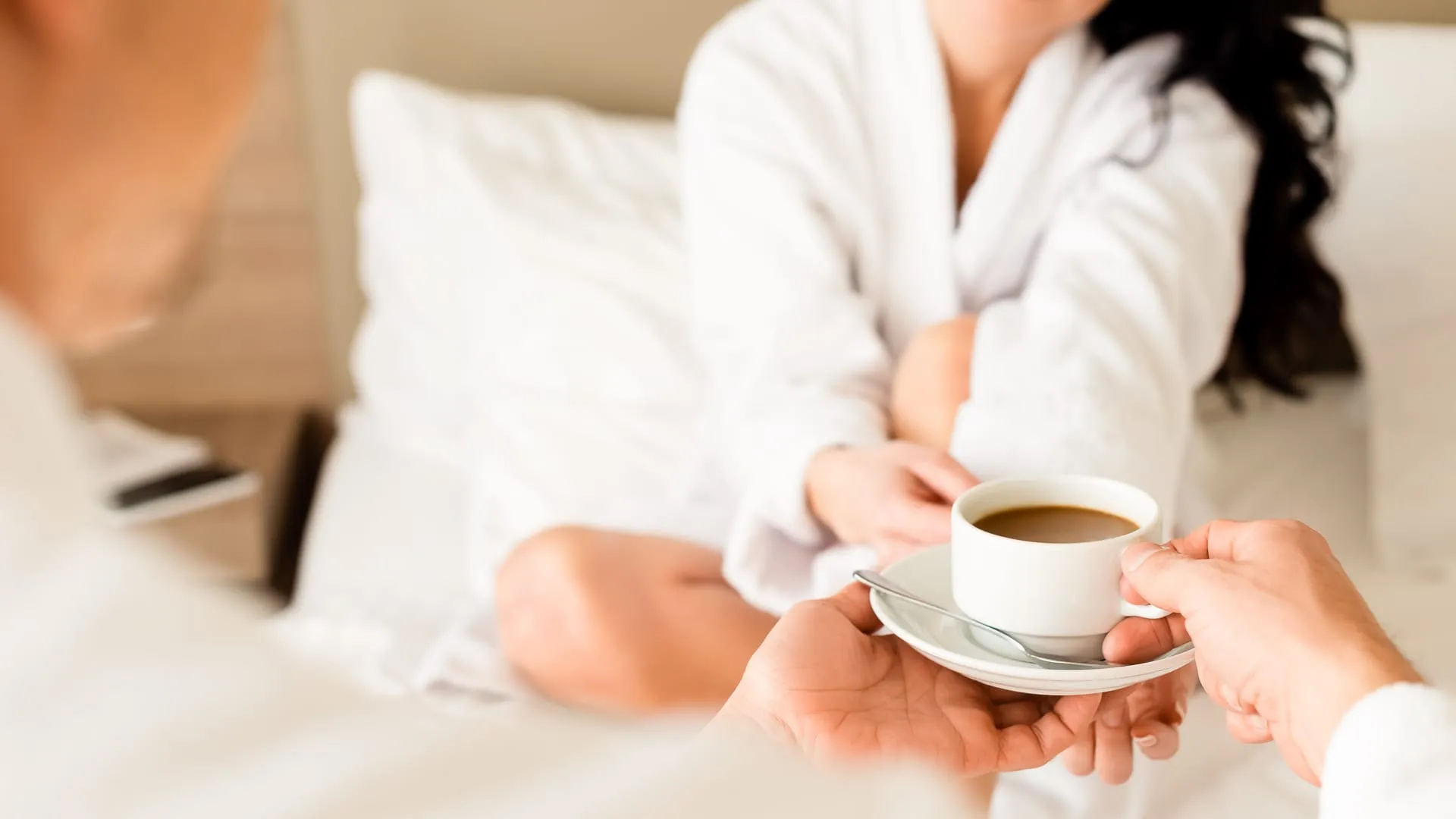 People in bed with bathrobes drinking coffee.