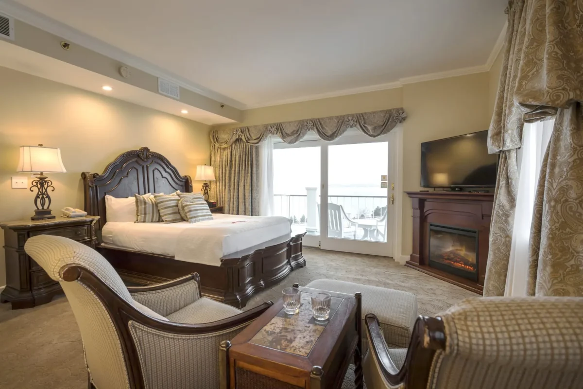 View of hotel bedroom with twin chairs and bed with view of balcony on the lake.