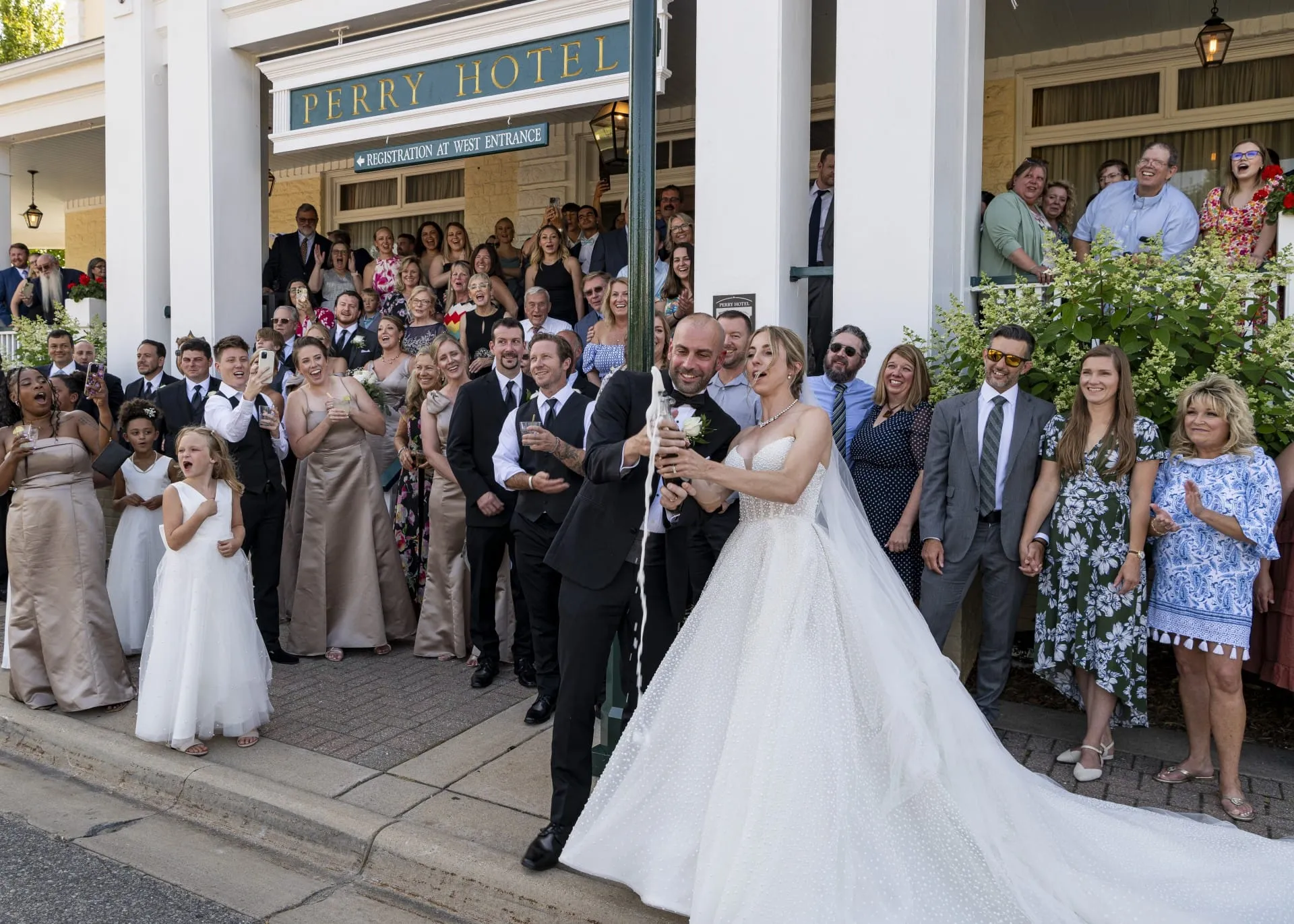 Bride and Groom Popping Champagne In front of large group of people.