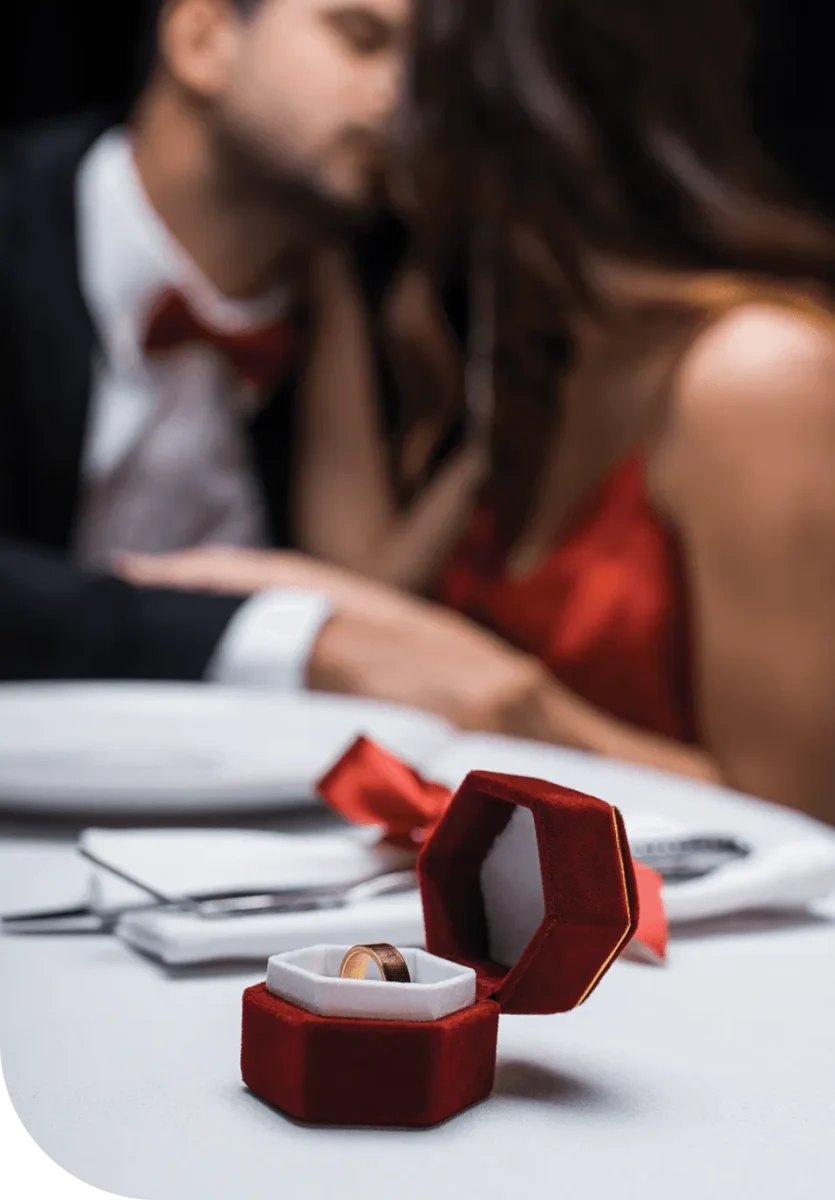 A bride a and a groom in the background with a engagement ring in the foreground.